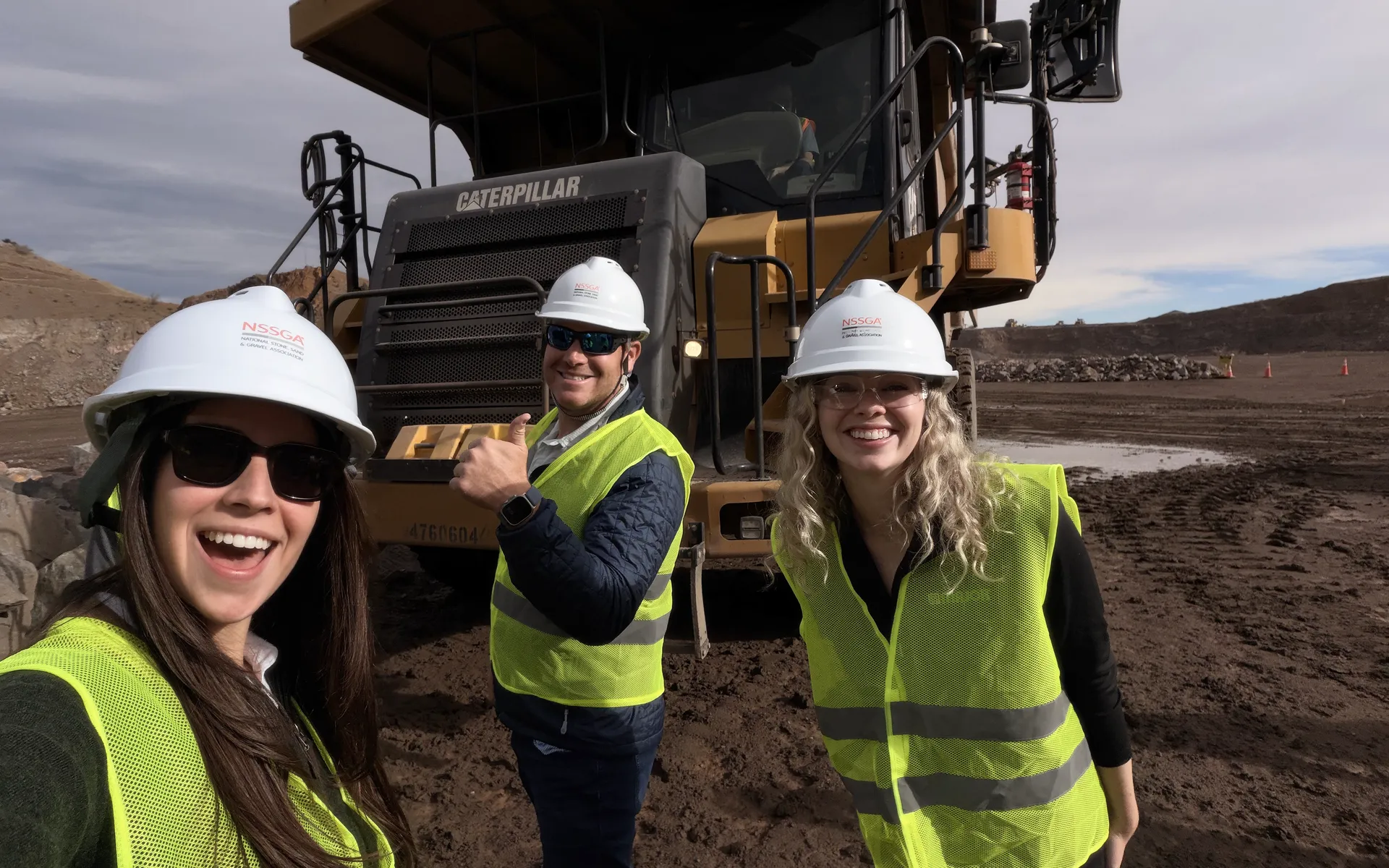 Clementina Davila and two other Young Leaders in hard hats in front of a Caterpillar haul truck
